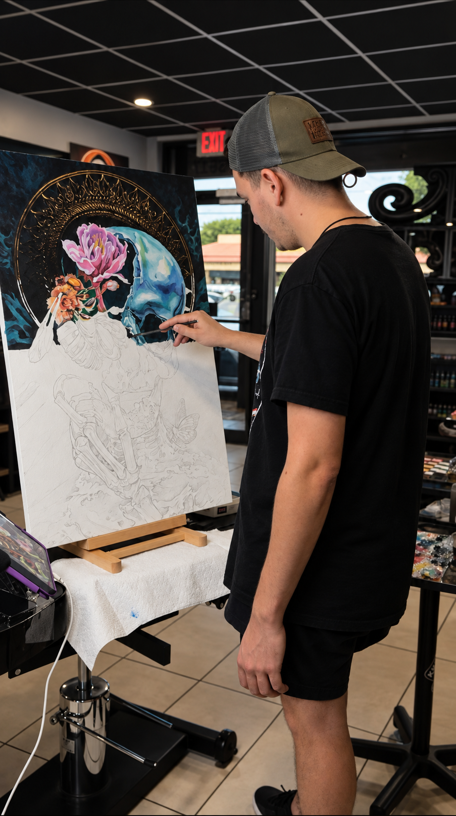 Yorlandi Fabregas painting the blue skull composition at an easel, with pencil outlines still visible.