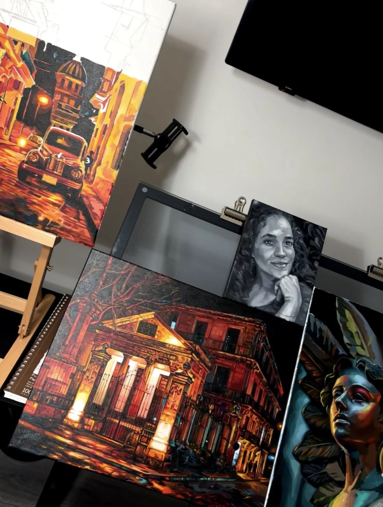 Studio view with nocturnal architectural paintings, a monochrome portrait and a colorful figurative painting.