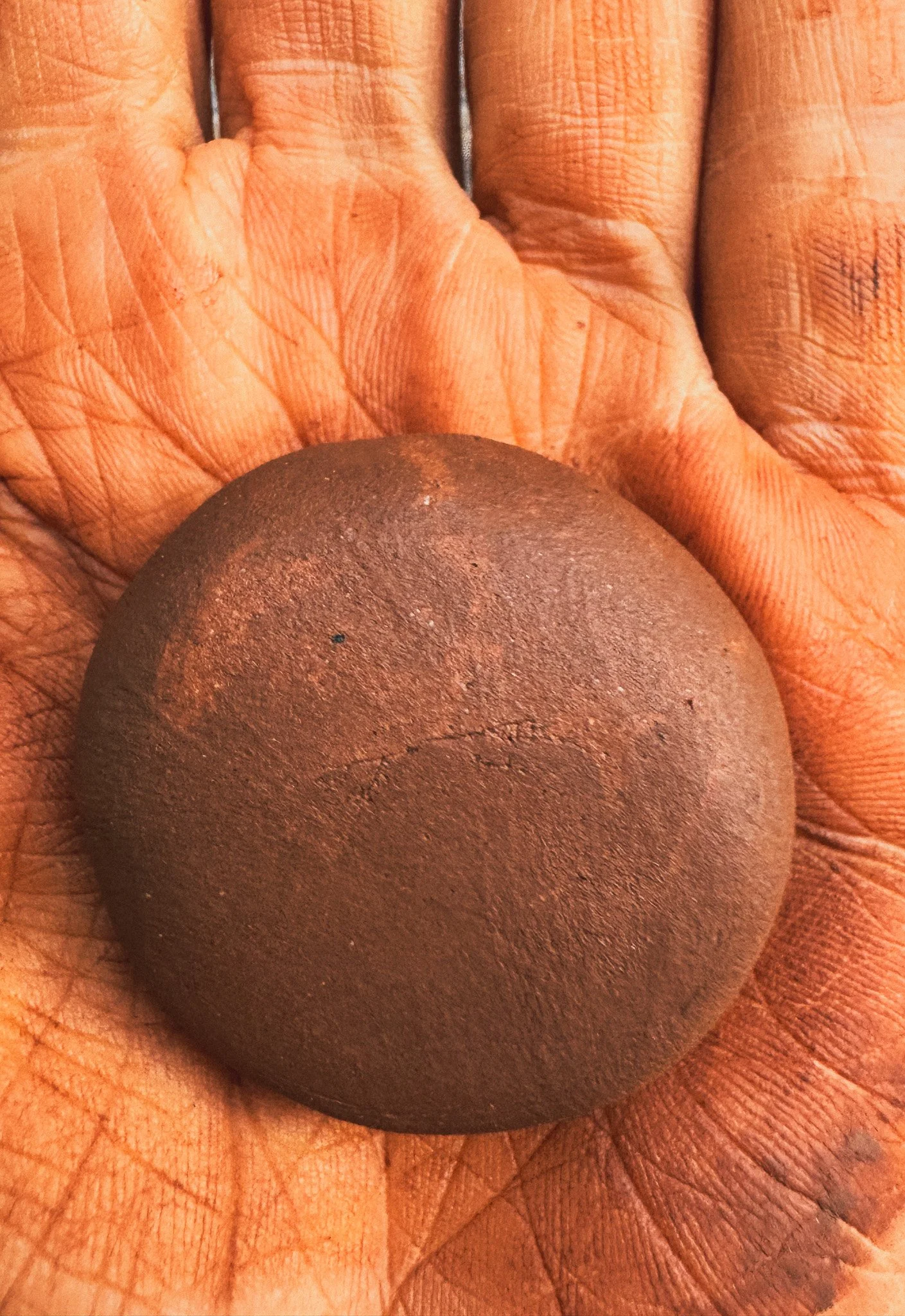 A rolled sphere of red clay cradled in a clay-dusted palm