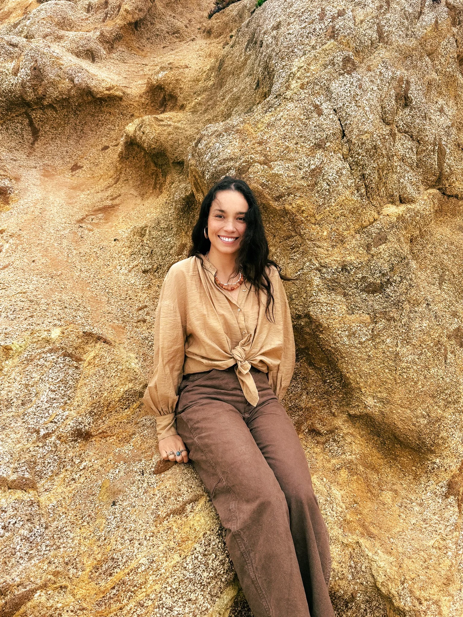Kristen Jael Acosta seated against desert rock, wearing a clay bead necklace