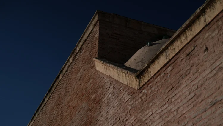 Angular red brick walls and a partial dome rise against a deep blue sky in Adana, Türkiye.