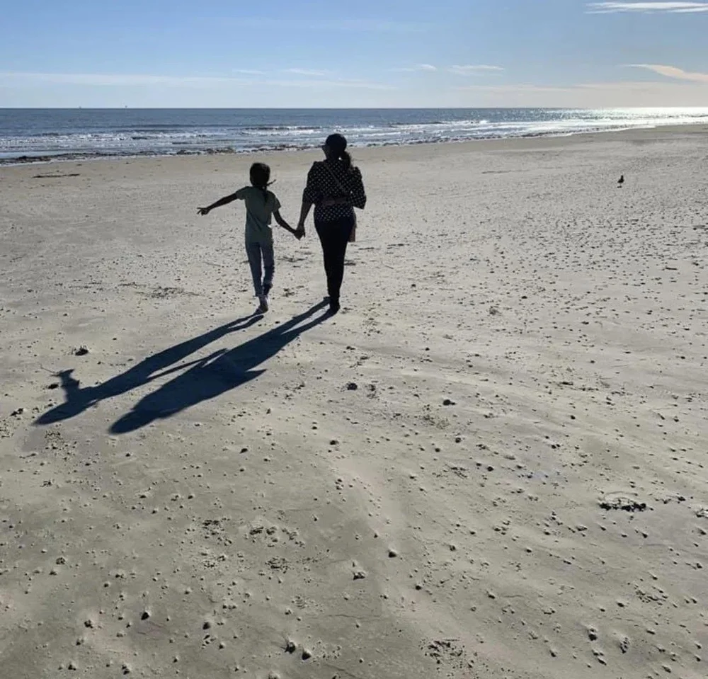 An adult and child walking hand in hand along a sunlit beach