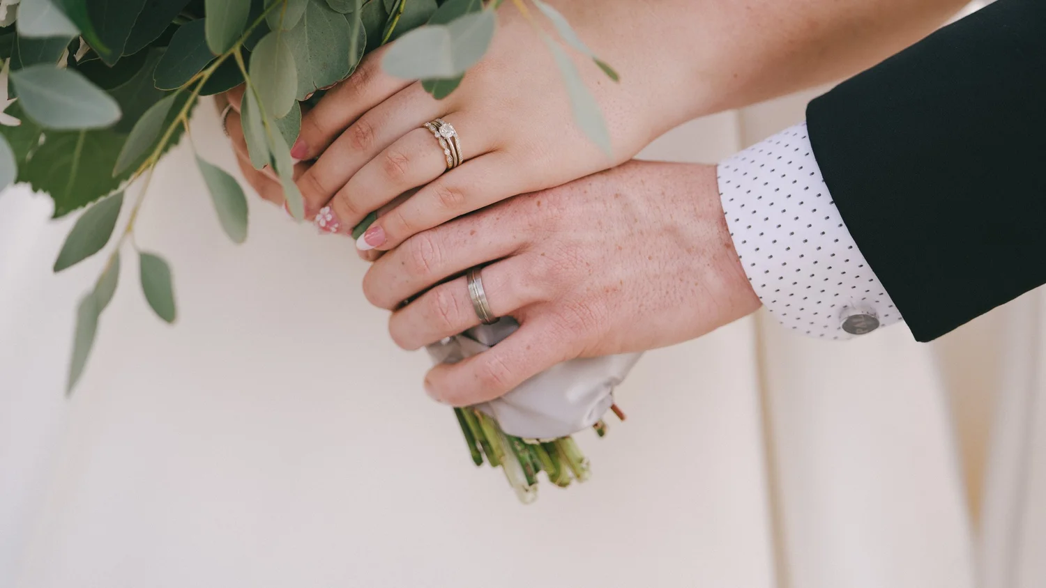Bride and groom hands with wedding rings over a bouquet