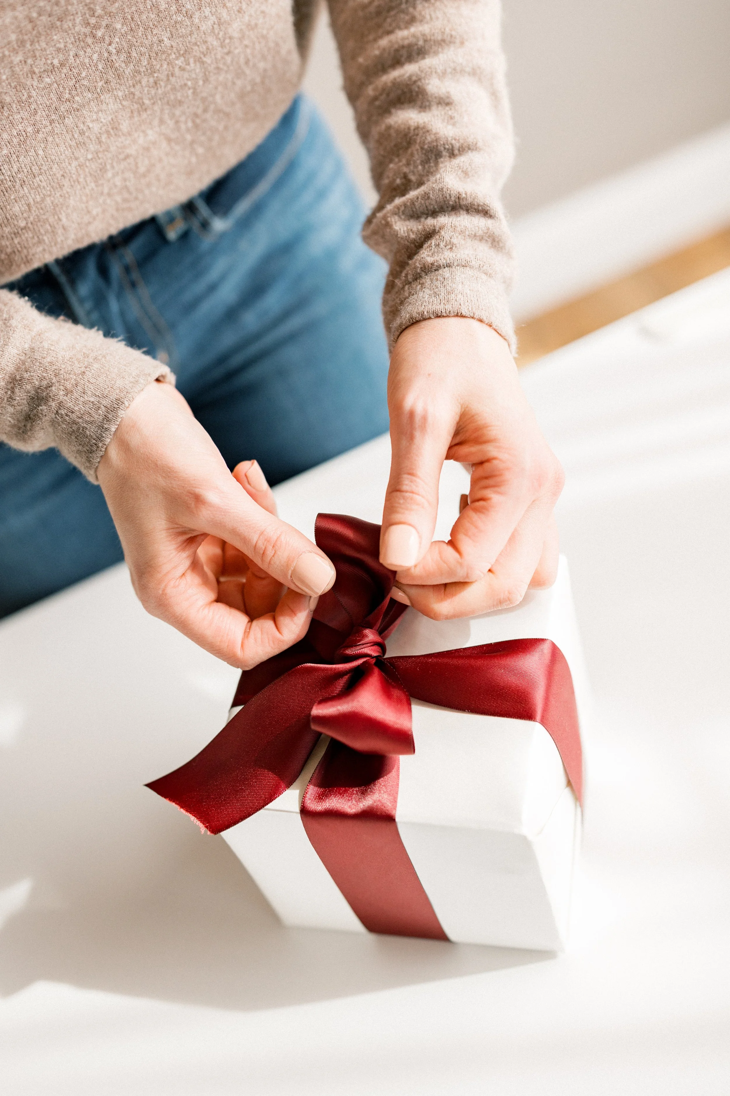 Hands tying a red bow on a white gift box