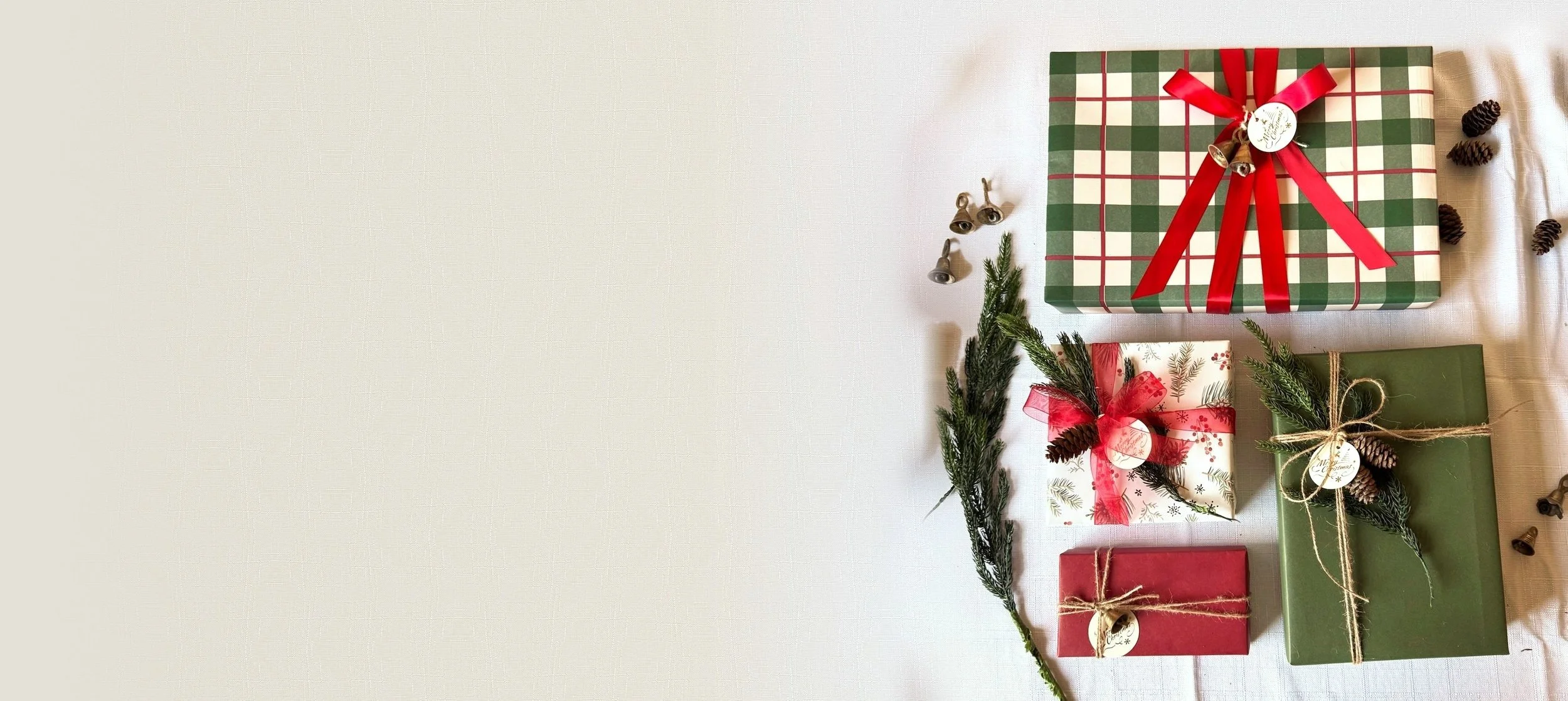 A group of Christmas gifts wrapped in plaid, greenery and red ribbon