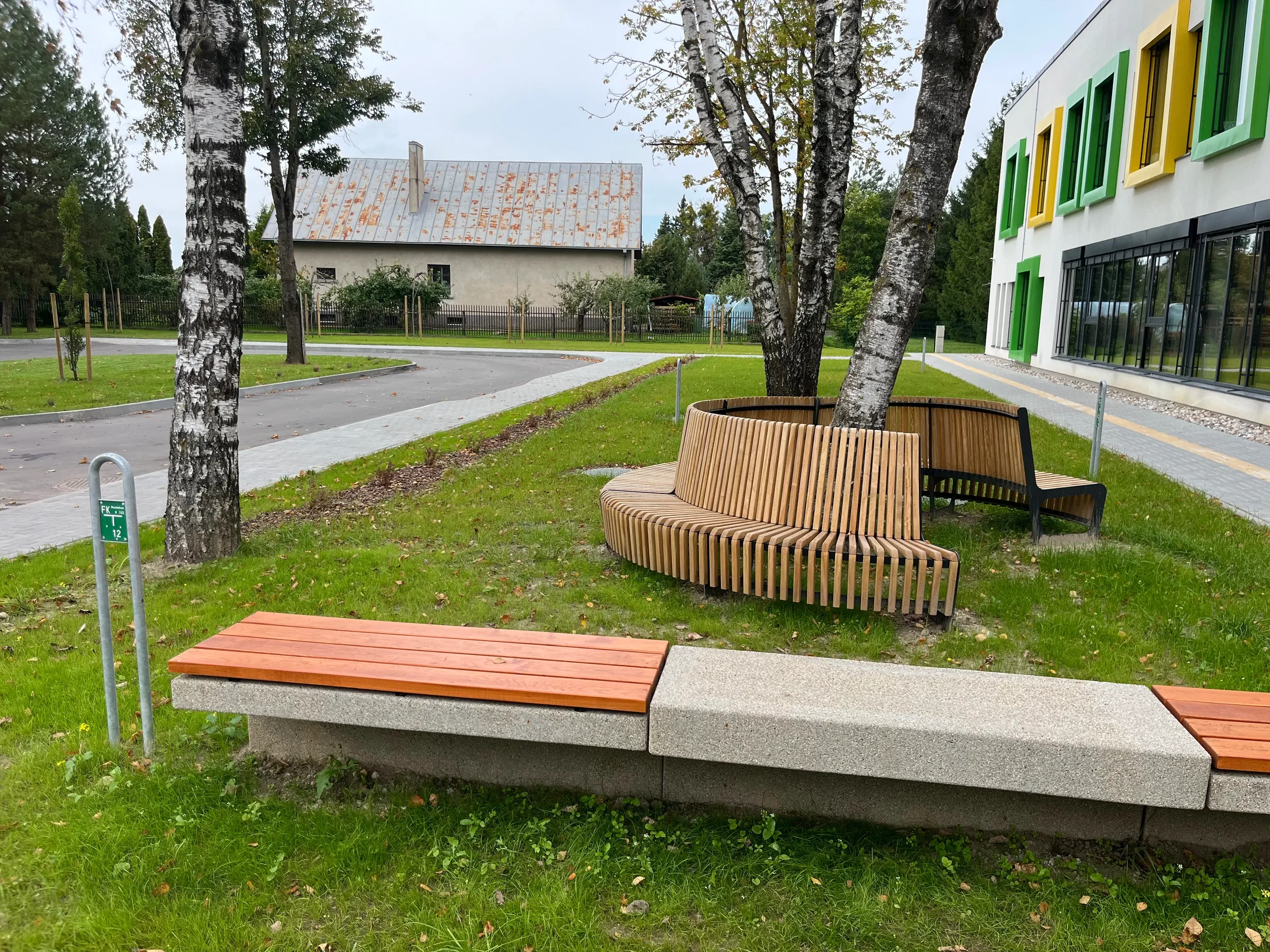 Apvali sėdimoji linija iš lenktų parko suoliukų po beržais