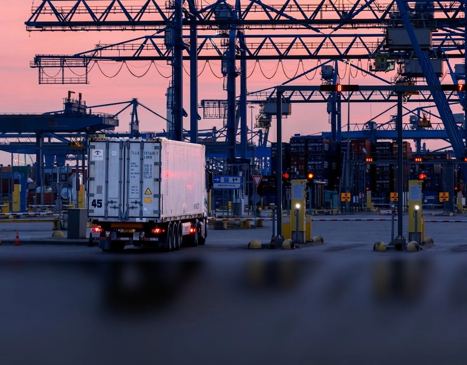 Lorry driving through a container port terminal gate at dusk