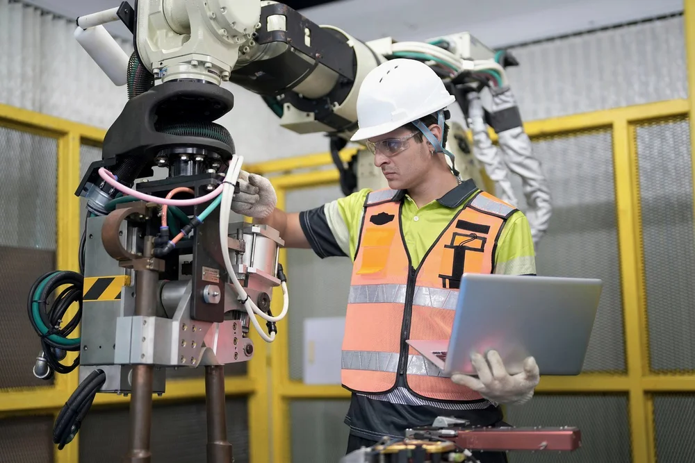 Engineer with a laptop servicing an industrial robot arm