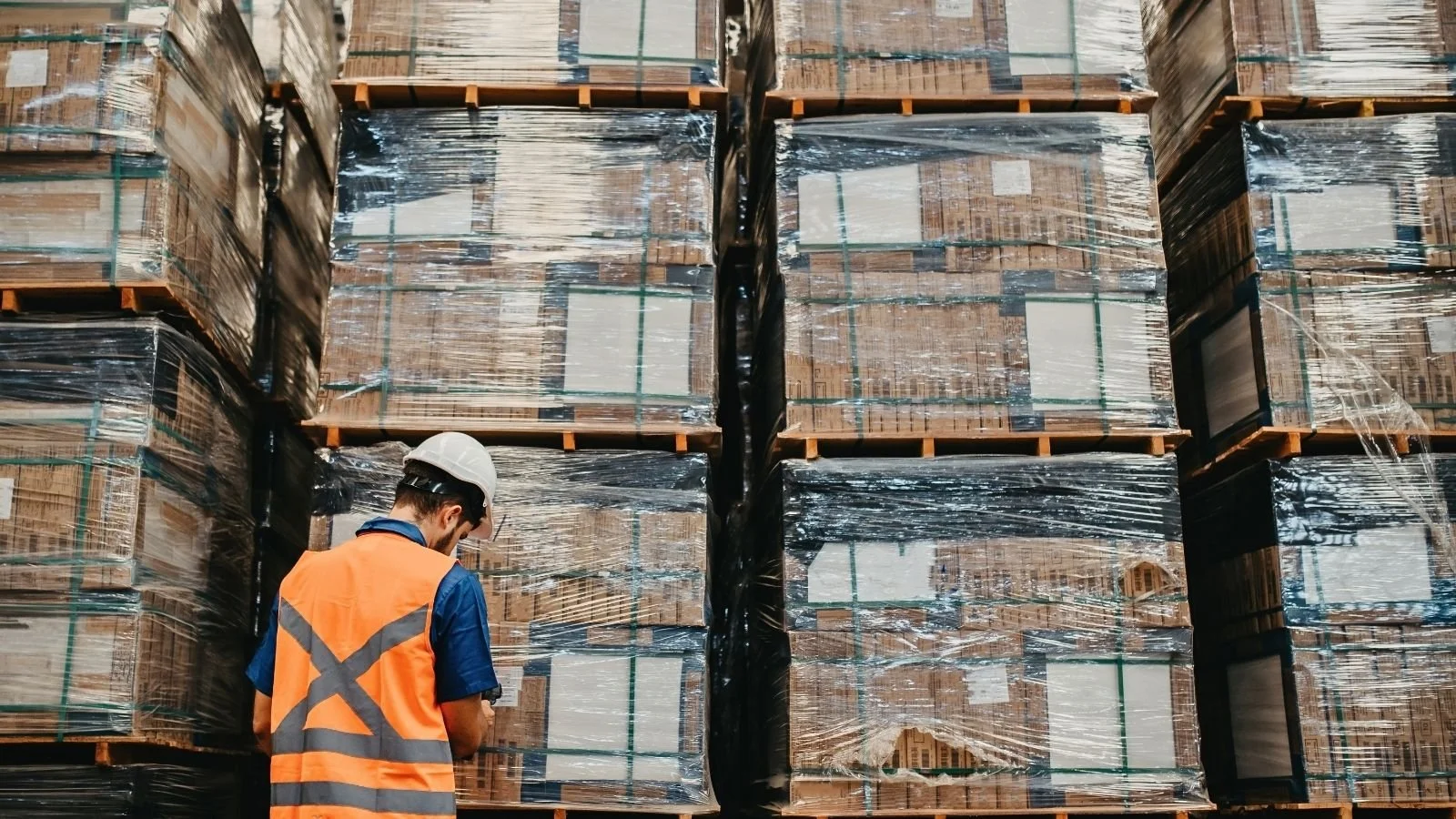 Warehouse worker checking shrink wrapped pallets of imported goods held in a bonded warehouse
