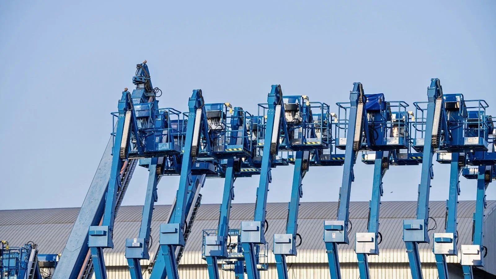 Row of boom lift access platforms held in stock at an equipment depot