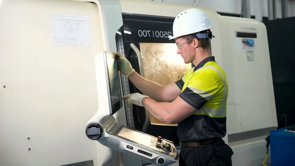 Engineer in a hard hat operating a CNC machine in a factory
