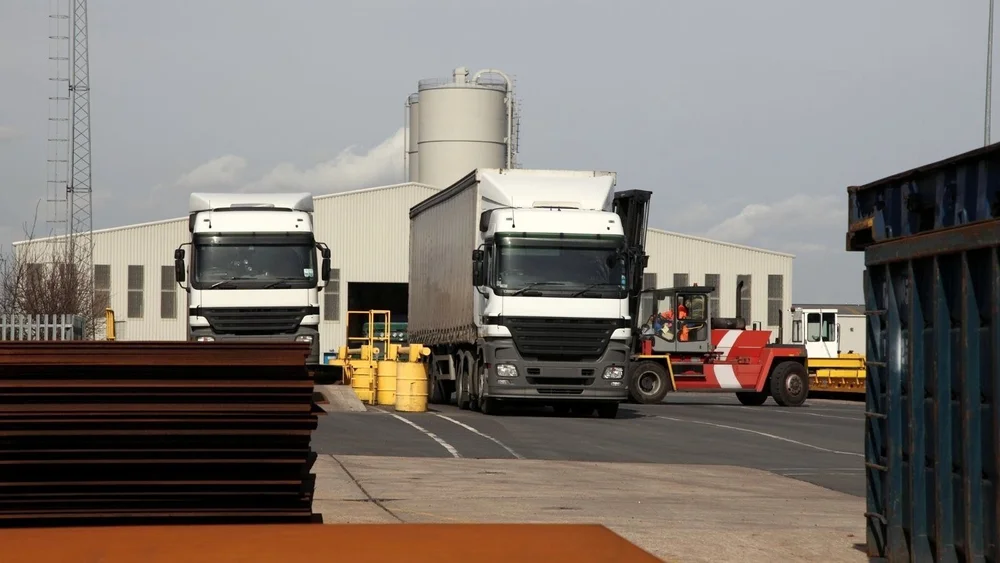 Two lorries and a forklift in a freight yard outside a warehouse