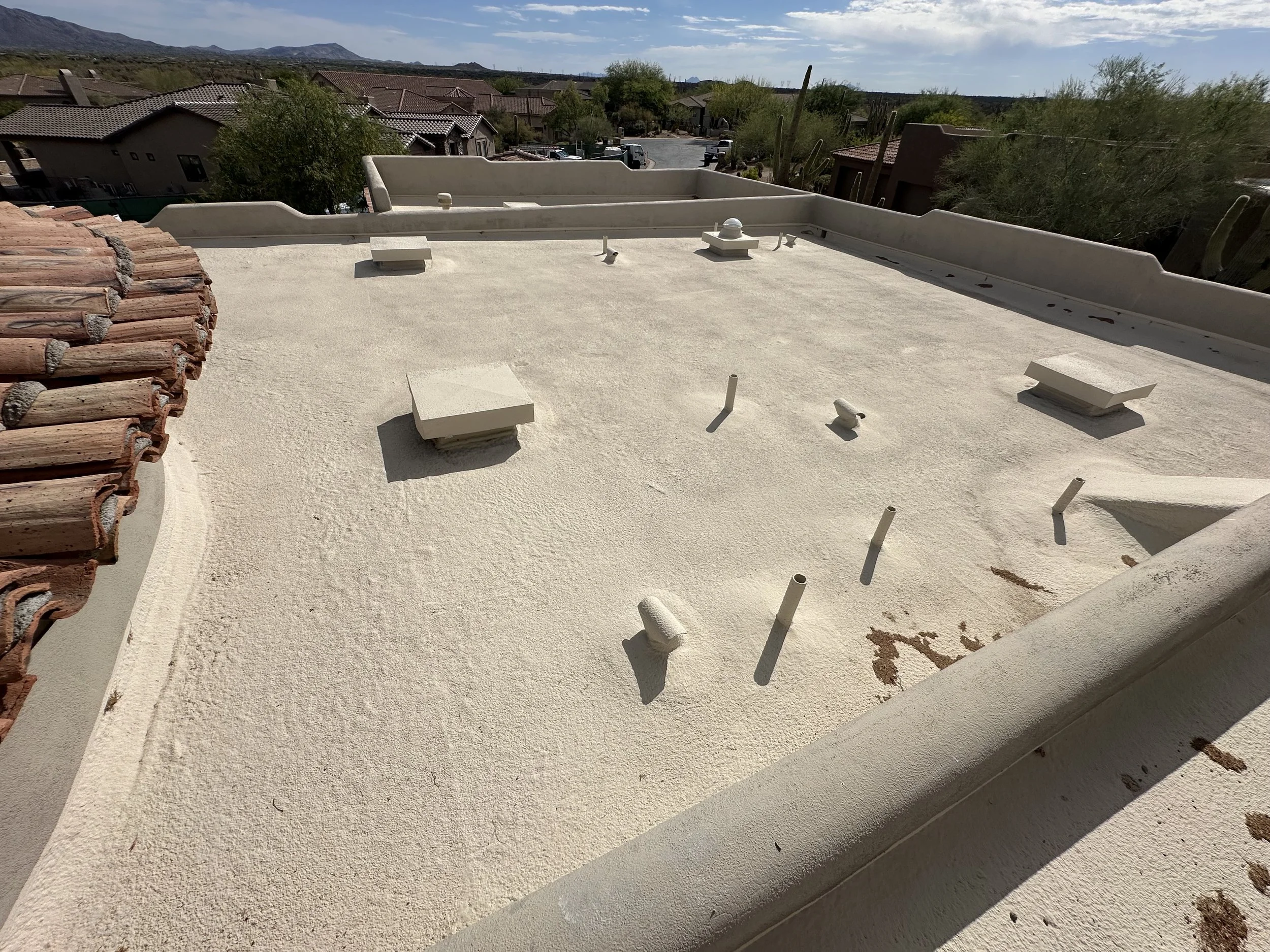 Flat foam roof with parapet wall and multiple roof vents on a North Scottsdale home, tile roofline and desert mountains in the background