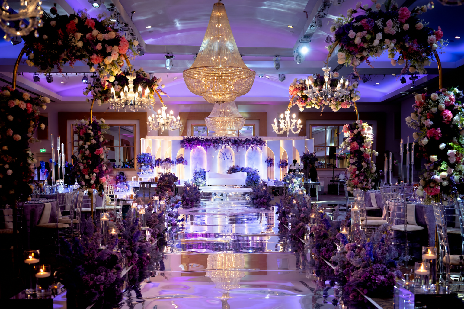 Floral arches and chandeliers frame a reception aisle