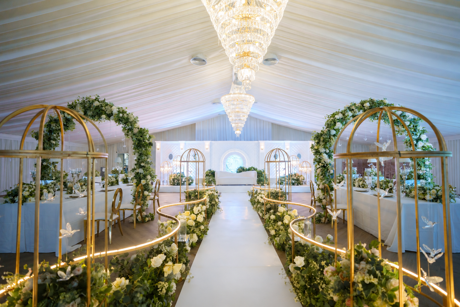 A white ceremony aisle framed by gold arches and green flowers