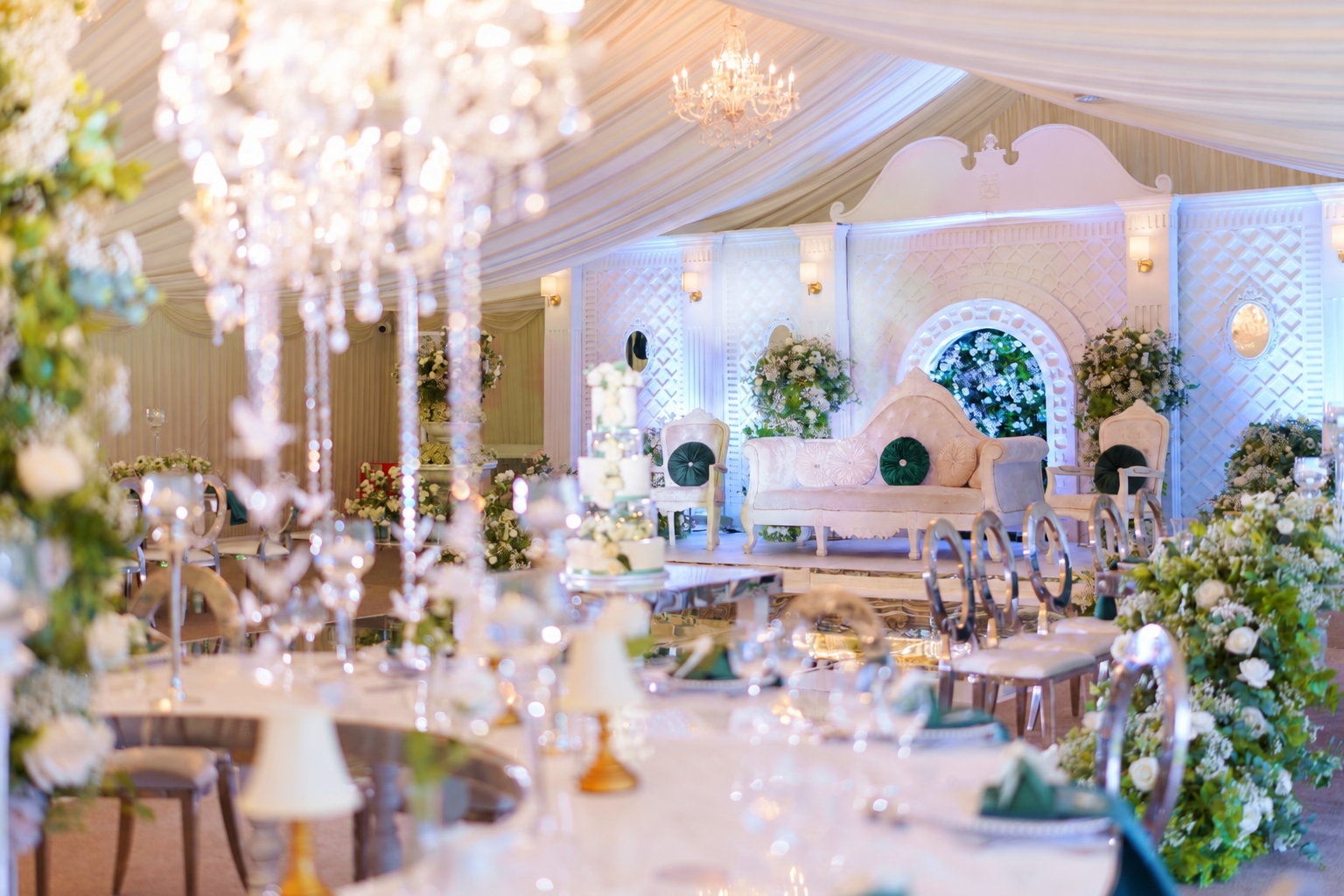 White and green wedding stage with chandeliers and floral tables