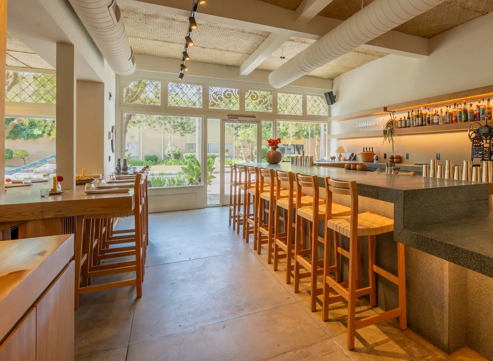 Warm, light-filled restaurant interior in Los Angeles with a long stone bar and wooden stools.