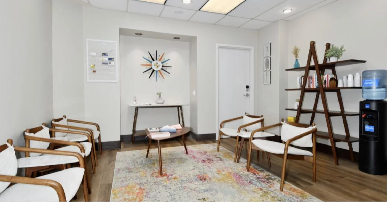 The calm shared waiting room in Suite 100 of the BP John Building in Johns Landing, Portland, with wood-framed chairs and a colorful rug