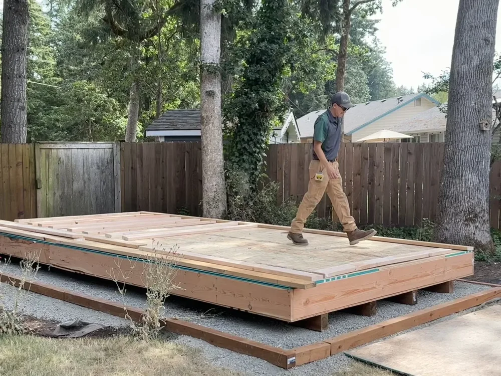 A ShedPro walking across the new floor system with wall framing laid out and the gravel pad below