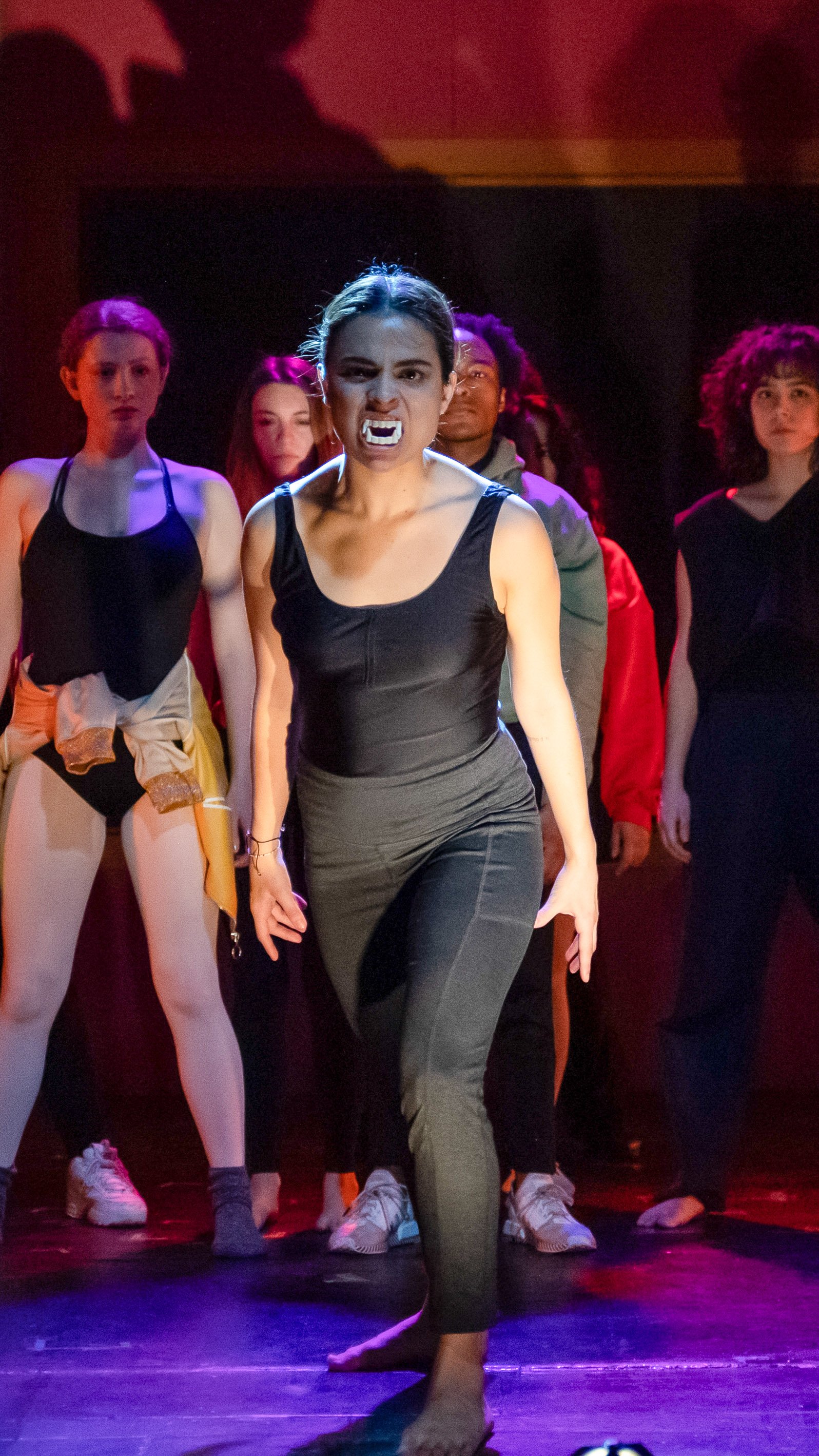 Dancer in black leads the ensemble under red and purple lighting in Dance Nation.