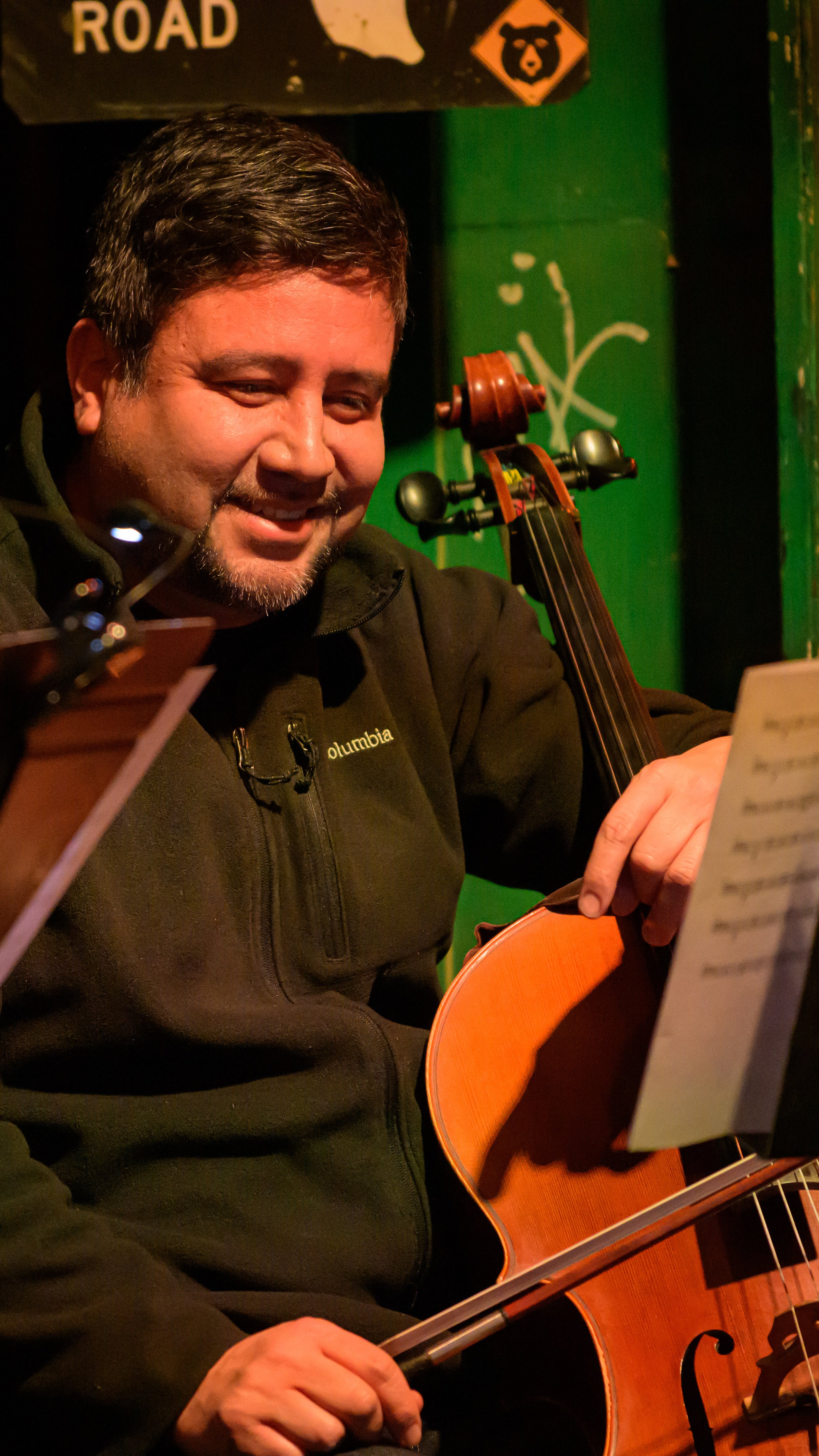 Cellist smiles while playing under warm stage lighting in Travelin’ Through.