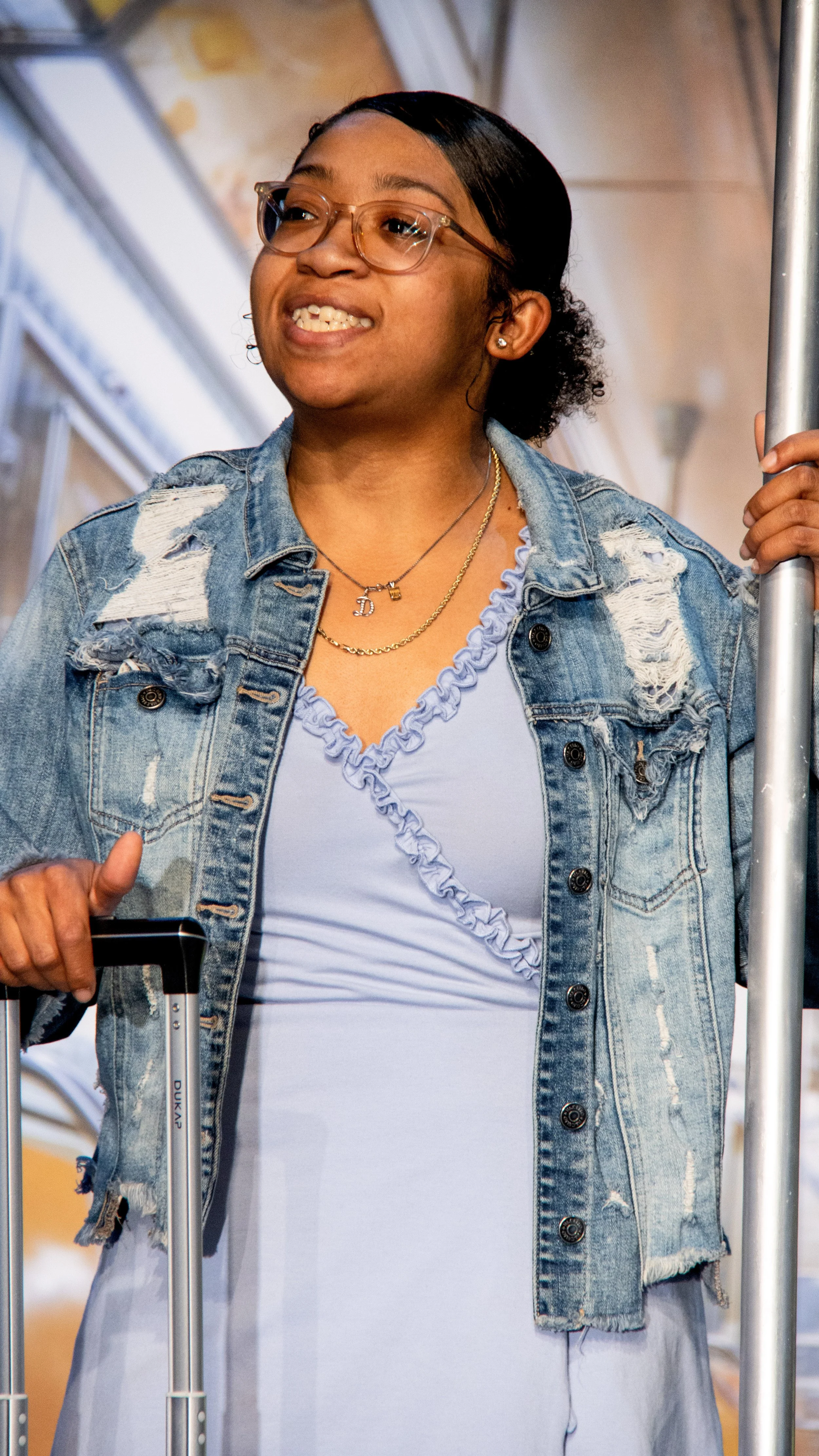 Performer in a denim jacket speaks into a headset microphone in Another Hundred People.