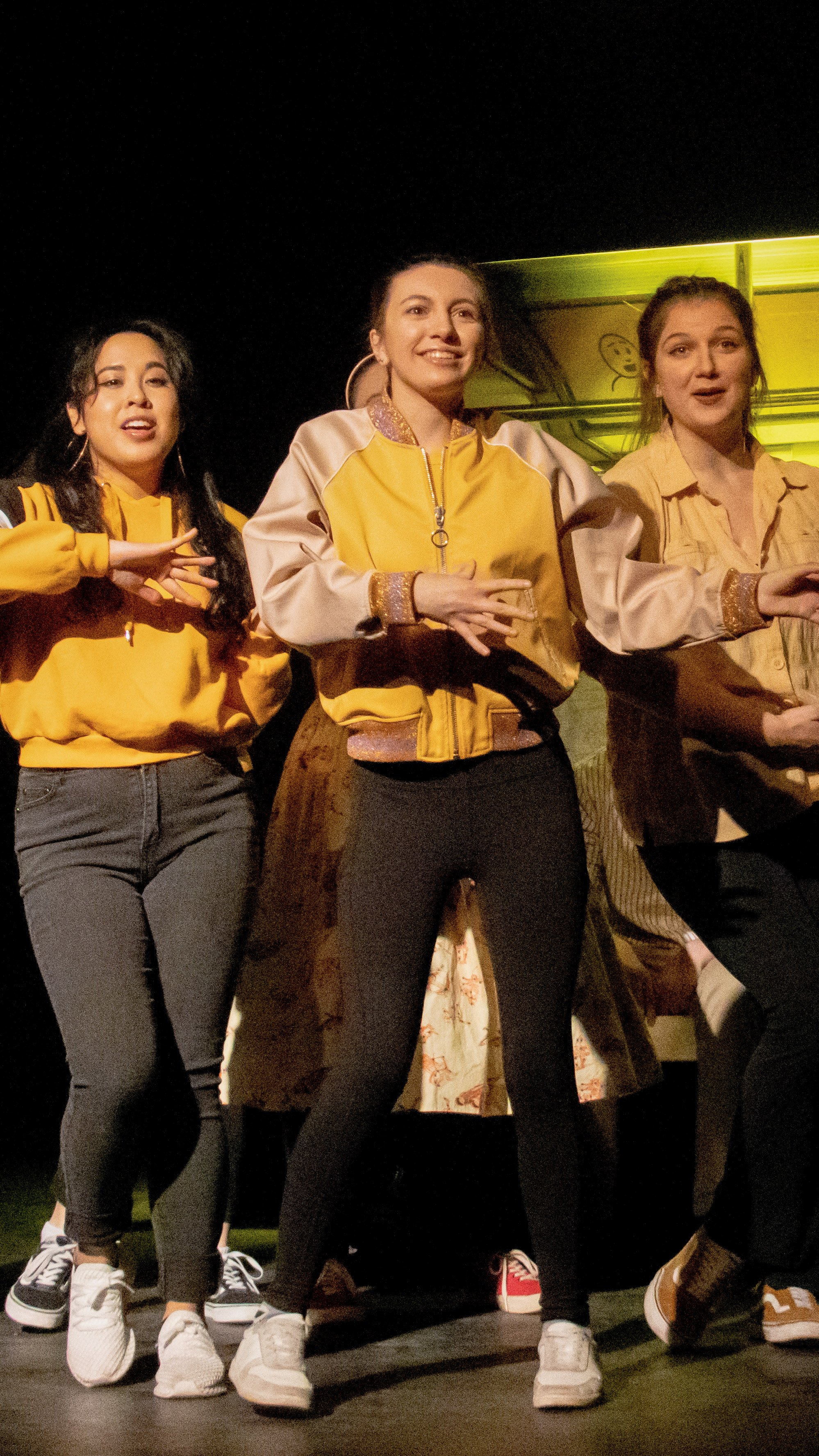 Three performers sing together in yellow and tan costumes in Another Hundred People.
