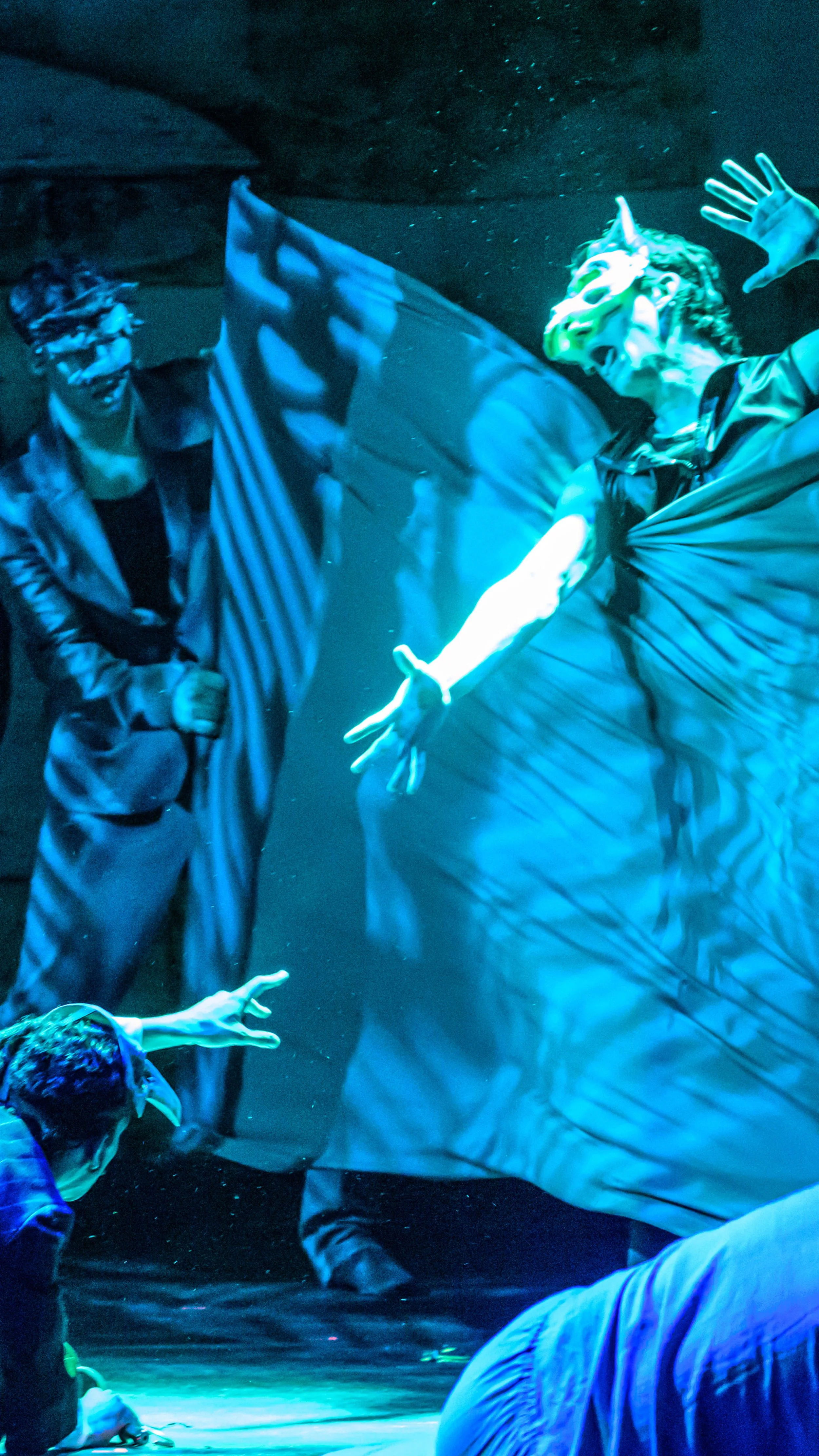 Ensemble surrounds a performer holding a large fabric panel under blue light in Mr. Burns.