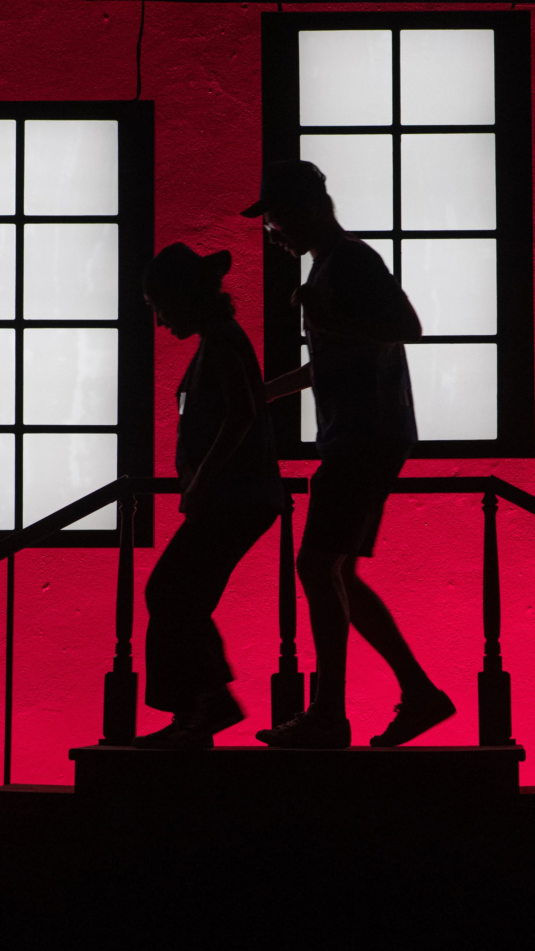 Silhouetted performers dance before red apartment windows in Stoop Songs.