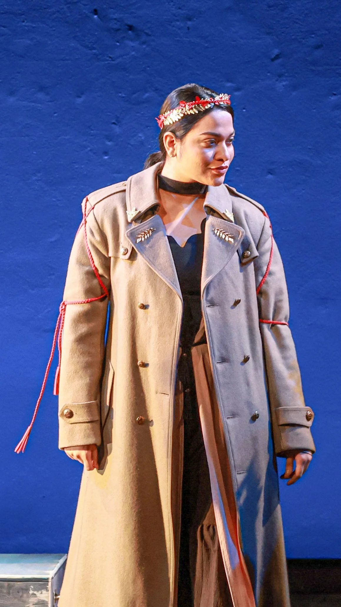 Performer in a long light-colored coat stands against a blue background in LEAR.