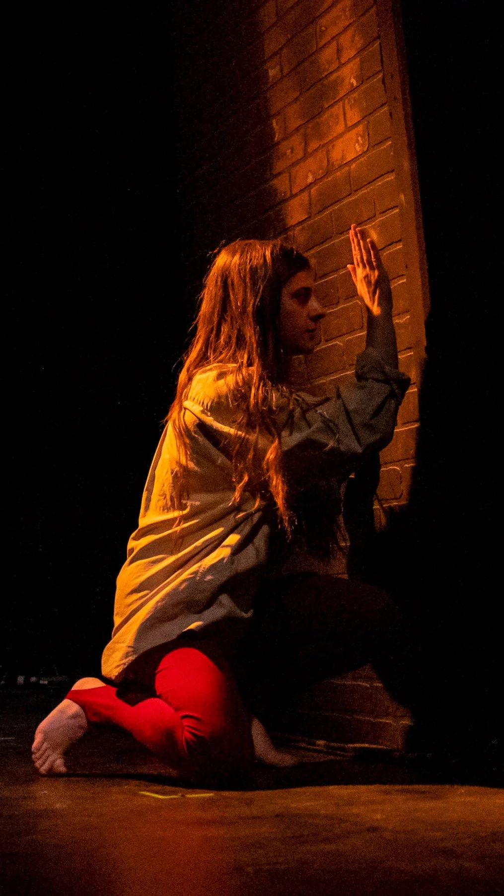 Performer crouches against a brick wall with one hand raised in Let the Right One In.