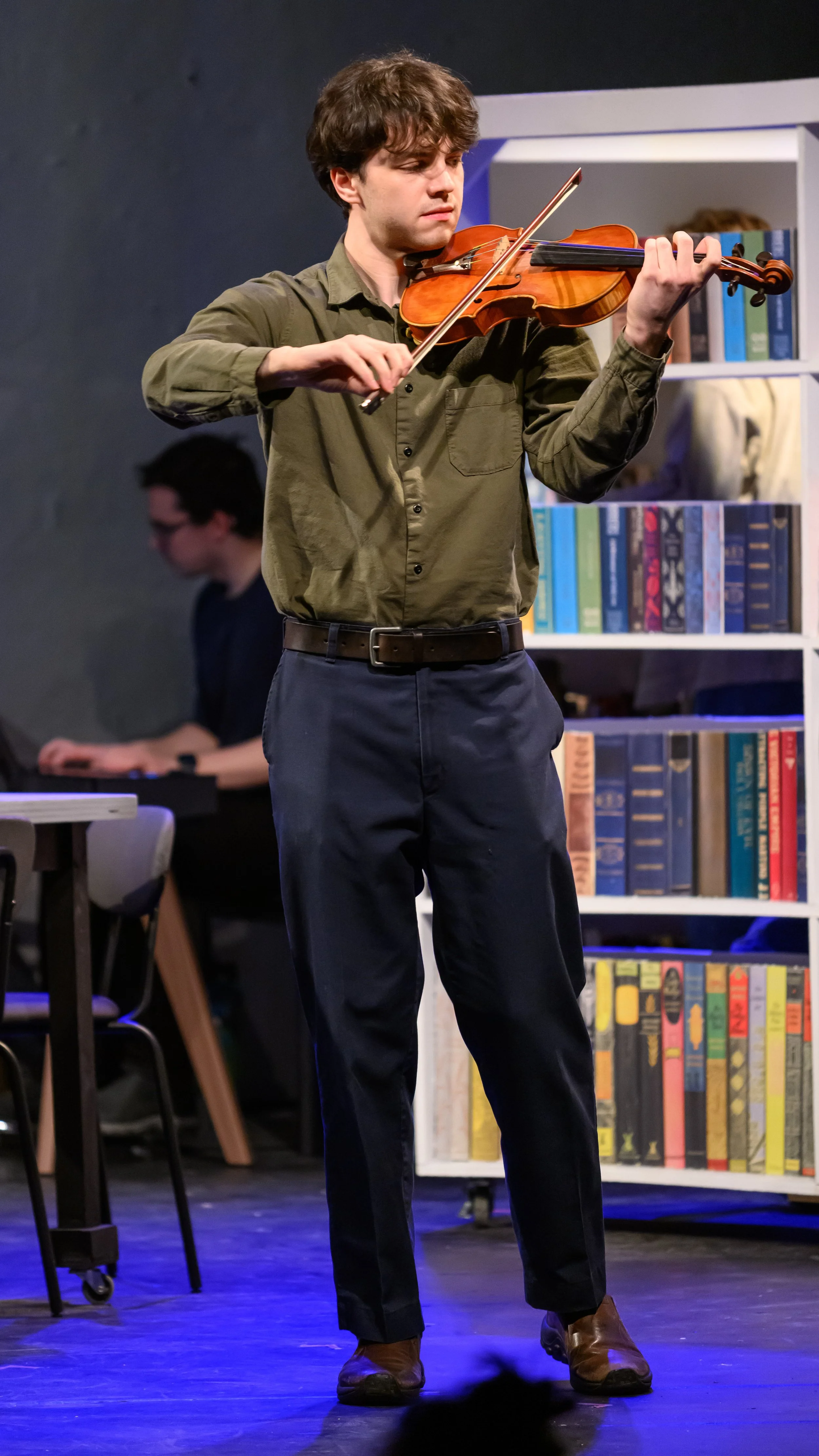 Performer plays the violin beside shelves of books in Pure Imagination.