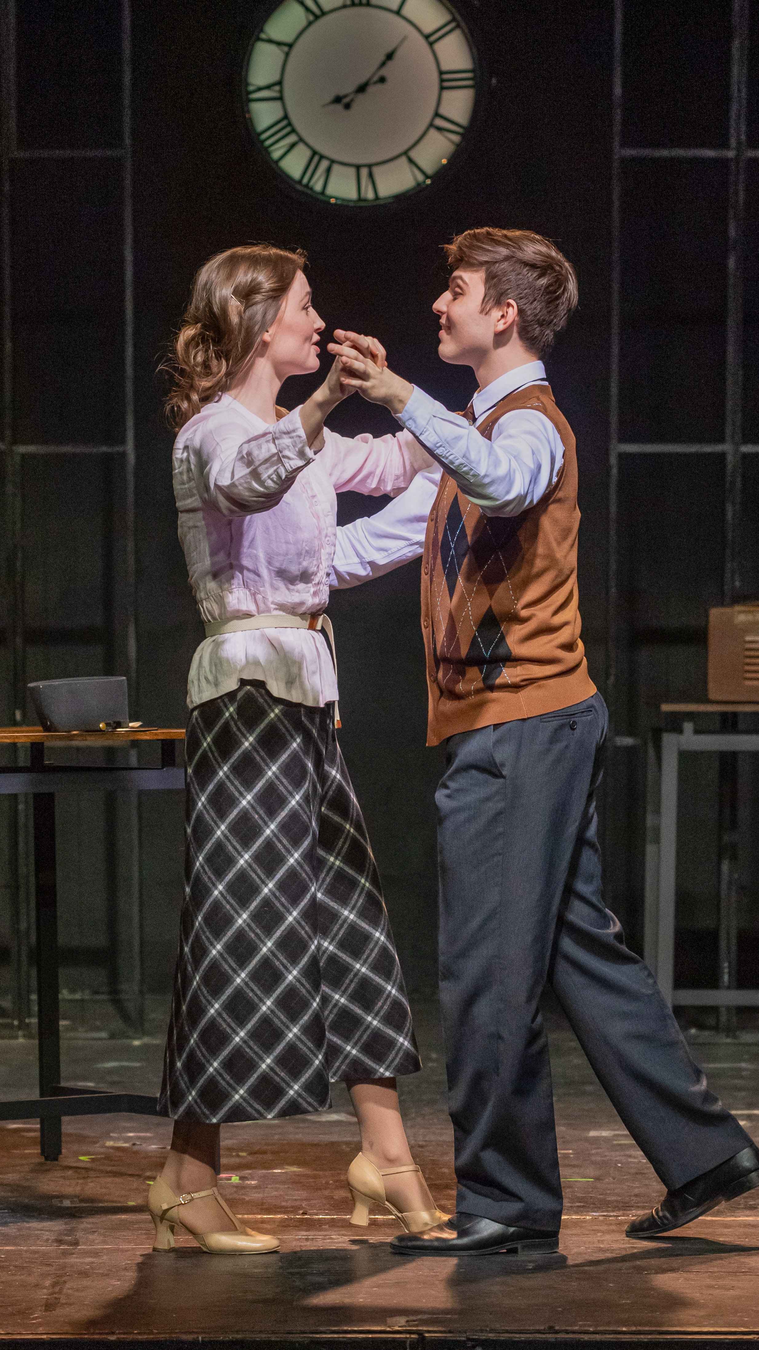 Two performers dance beneath a large wall clock in Radium Girls.