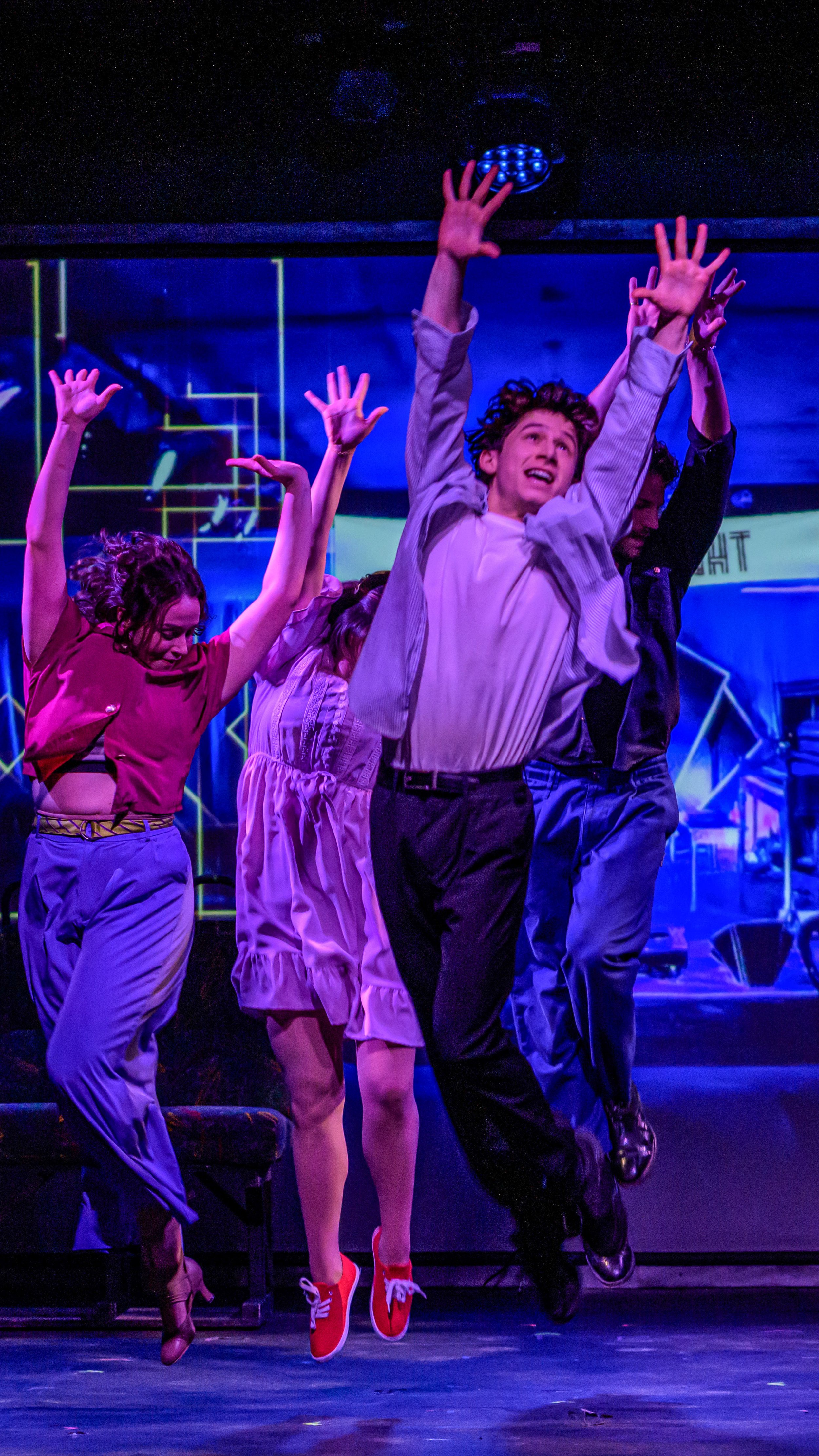 Three performers leap with arms raised under purple and blue lights in Travelin’ Through.
