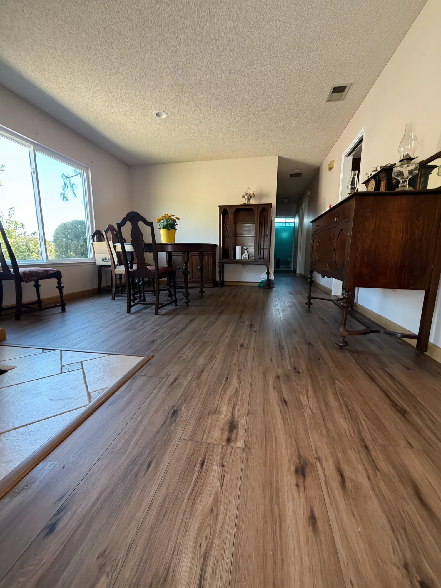 Warm wood-look plank flooring through a living and dining room with a sunny window and dark wood furniture