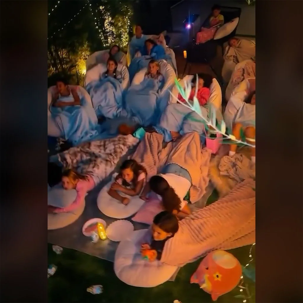 Kids relaxing on floor cushions and bean bags under blankets at a backyard movie night.