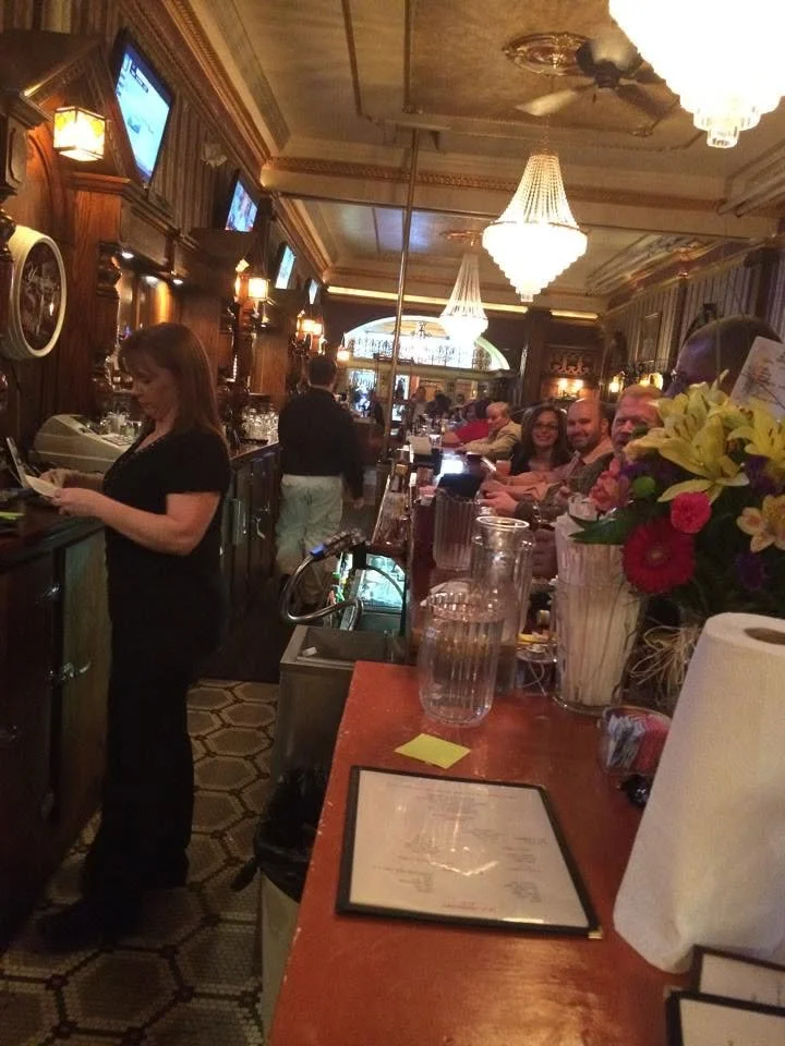 View along the wooden bar with hanging chandeliers and a vase of flowers.