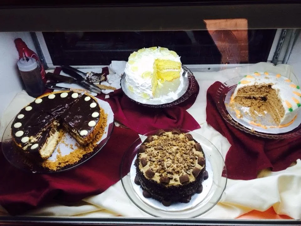 Several decorated cakes, some sliced, arranged in a dessert display.
