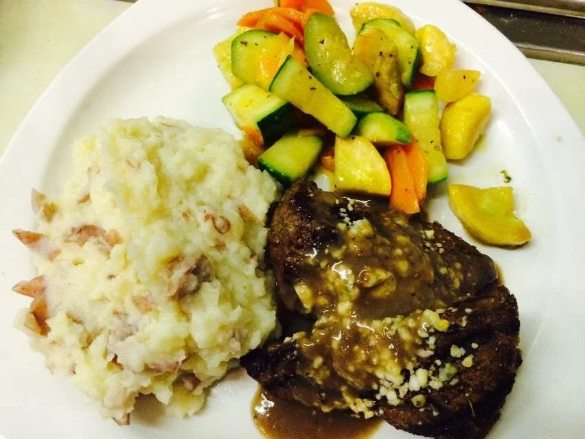 Browned entree with sauce, mashed potatoes and mixed vegetables.