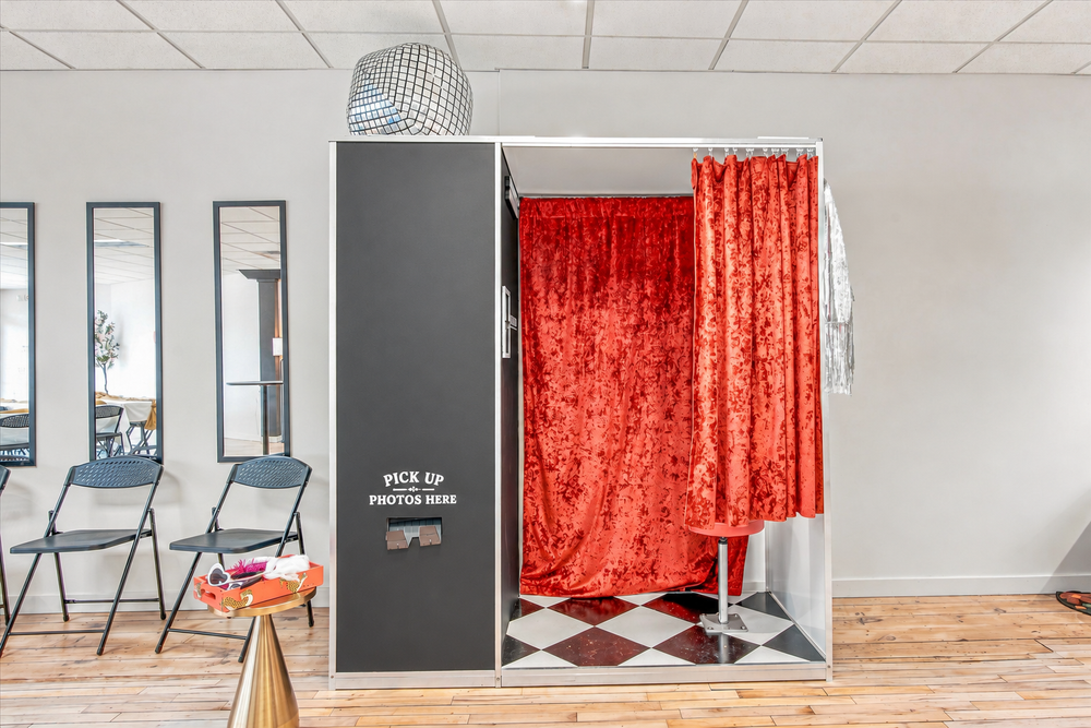 The Vow House photo booth with red velvet curtains, a disco ball, and printed photo pickup