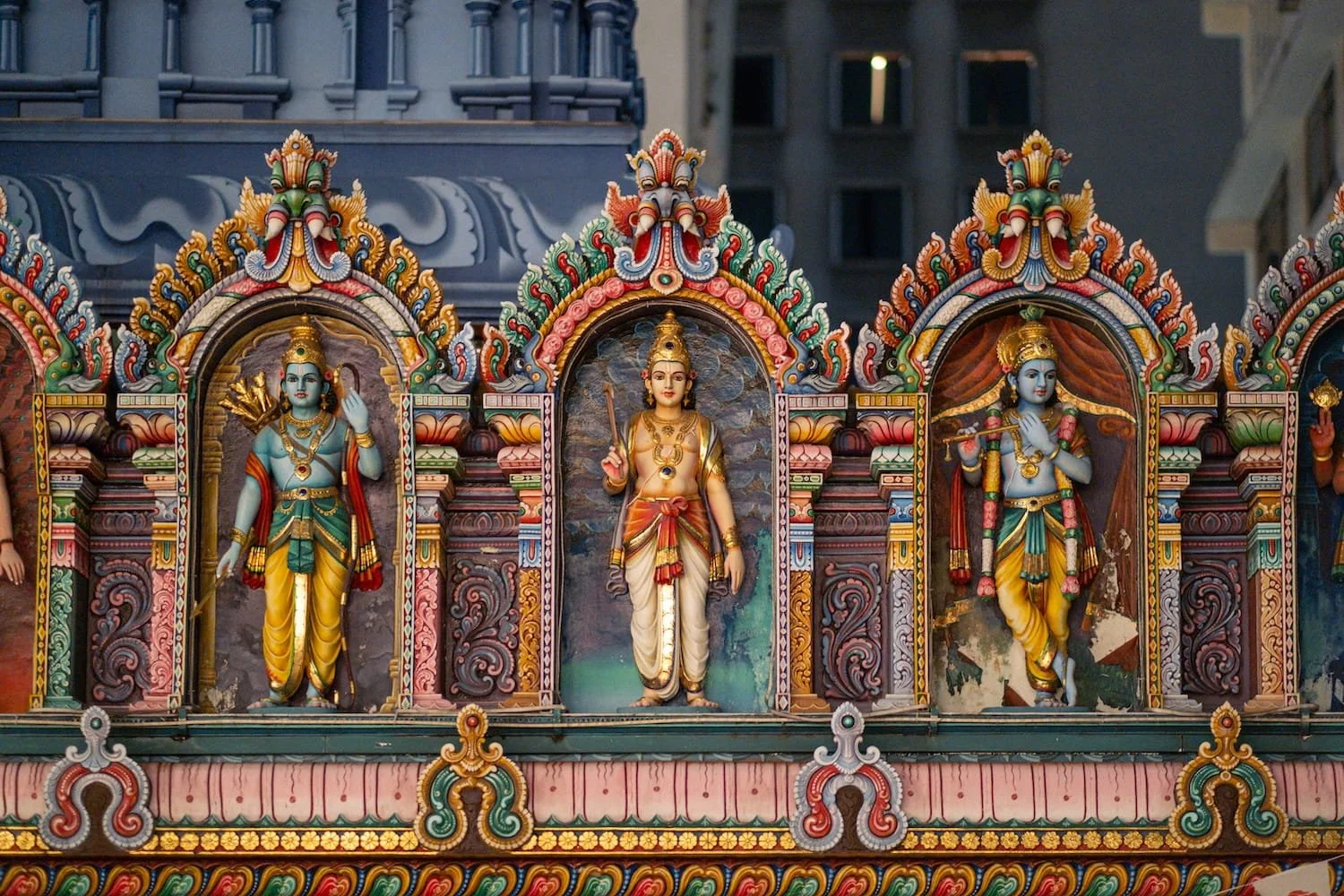 Colorful Hindu deity sculptures in ornate arched frames on Singapore temple facade