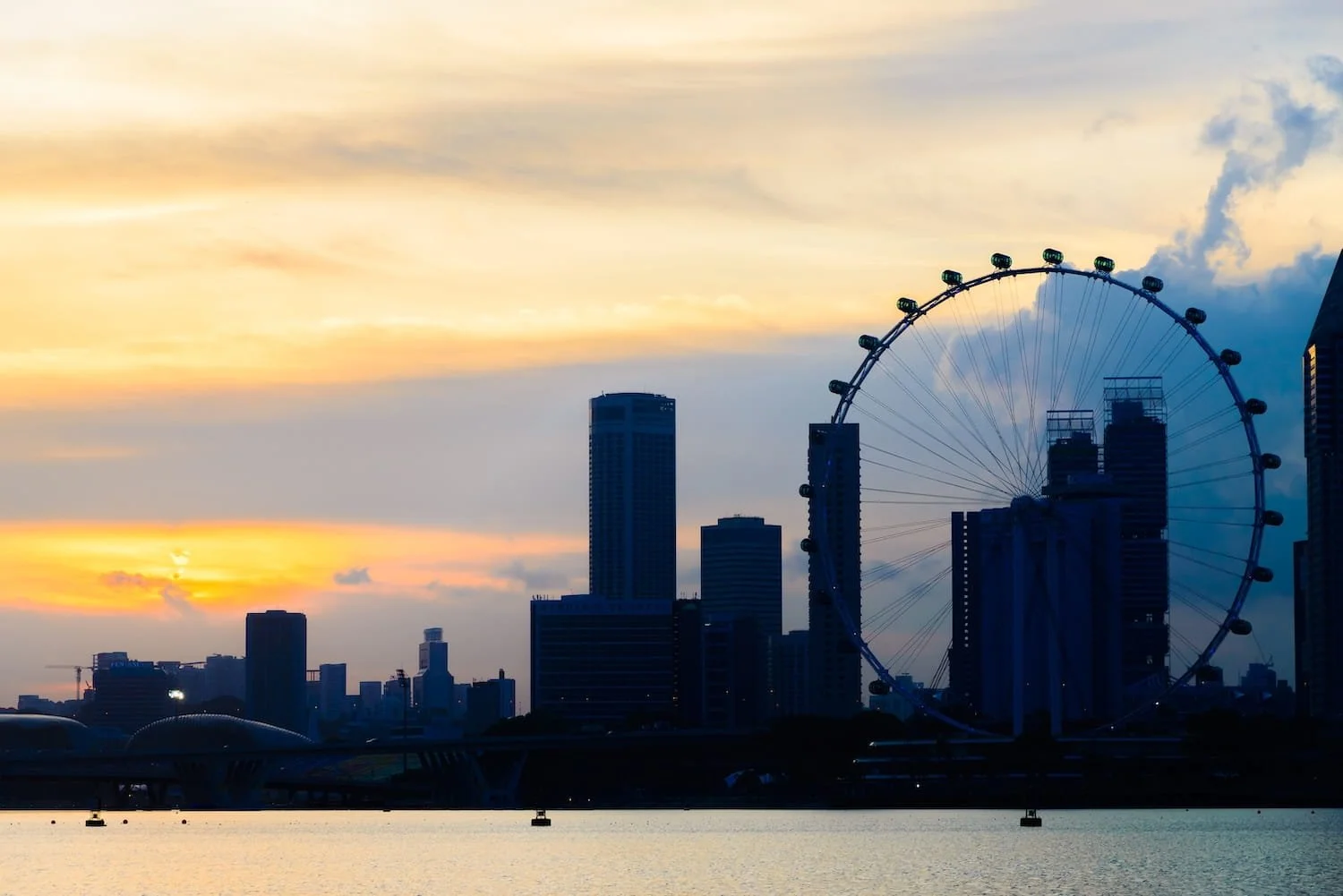 Singapore Flyer observation wheel silhouetted against golden sunset with modern city skyline