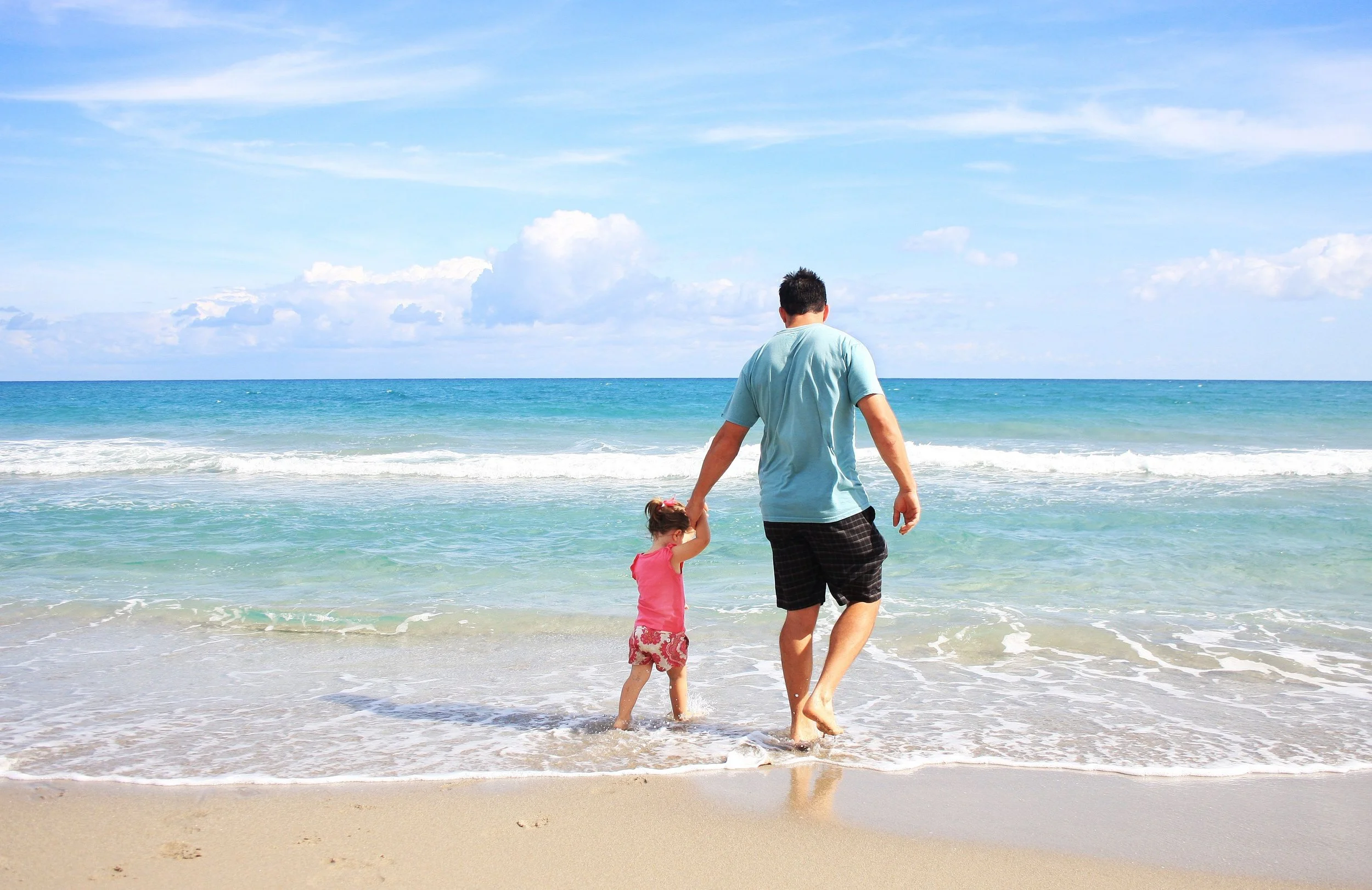A father and daughter holding hands while walking along a beach.