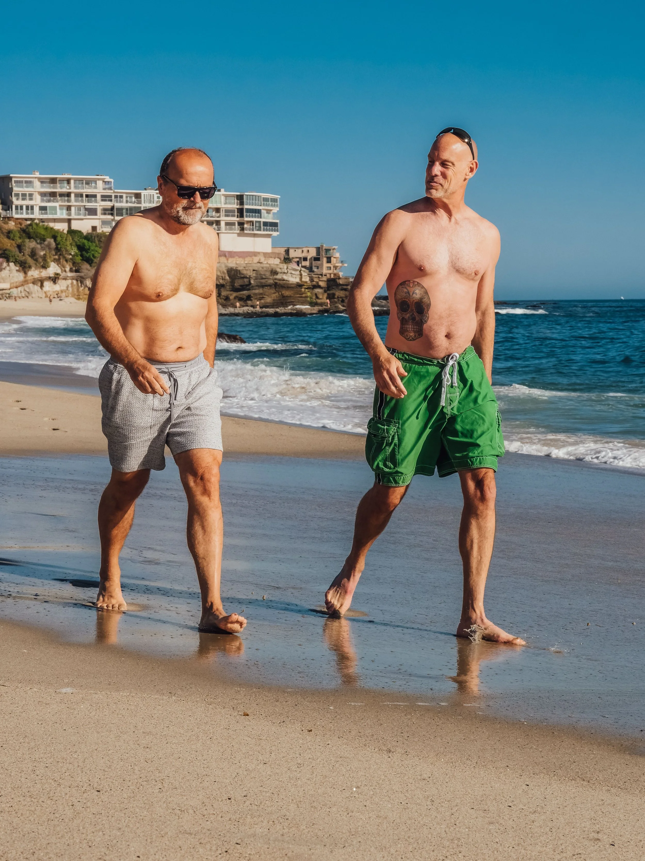 Two men walking together along the shoreline of a beach on a clear day