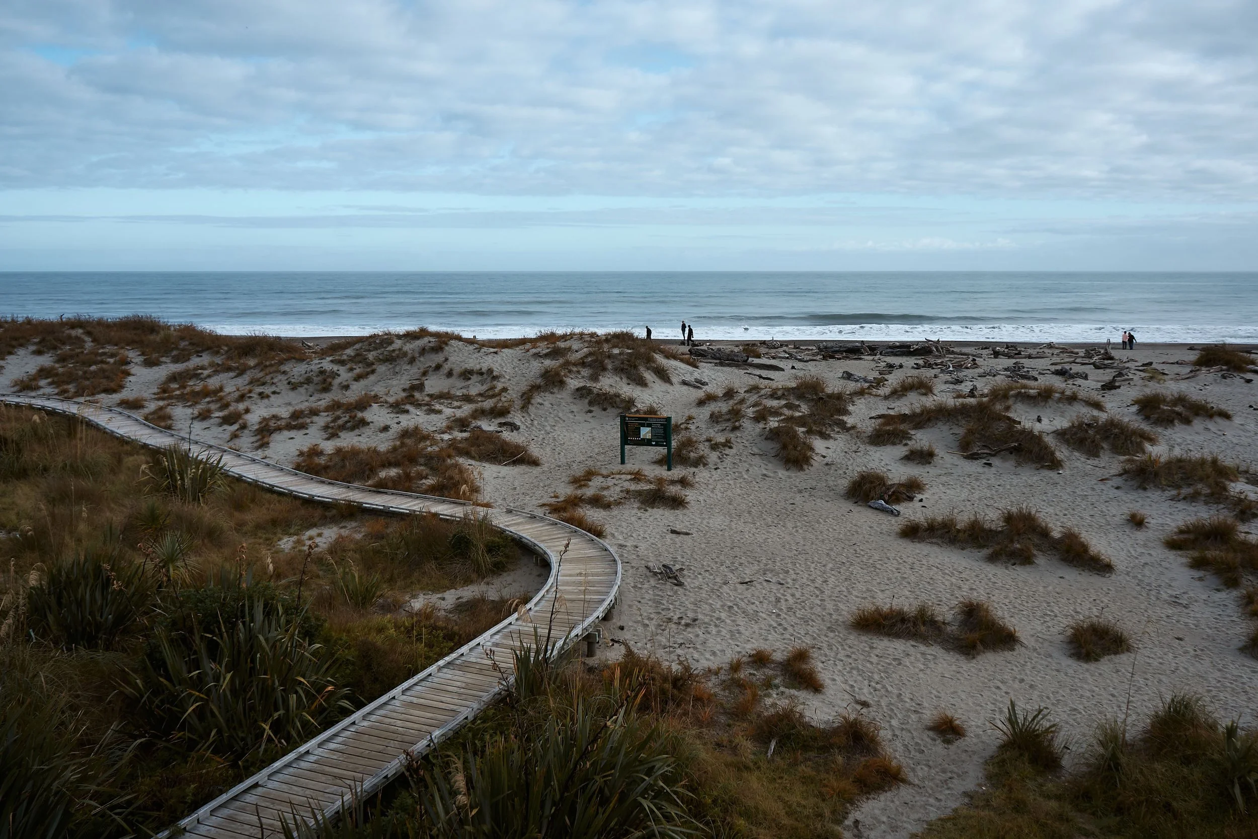 A wooden boardwalk leading through sand dunes towards a beach beneath a cloudy sky.