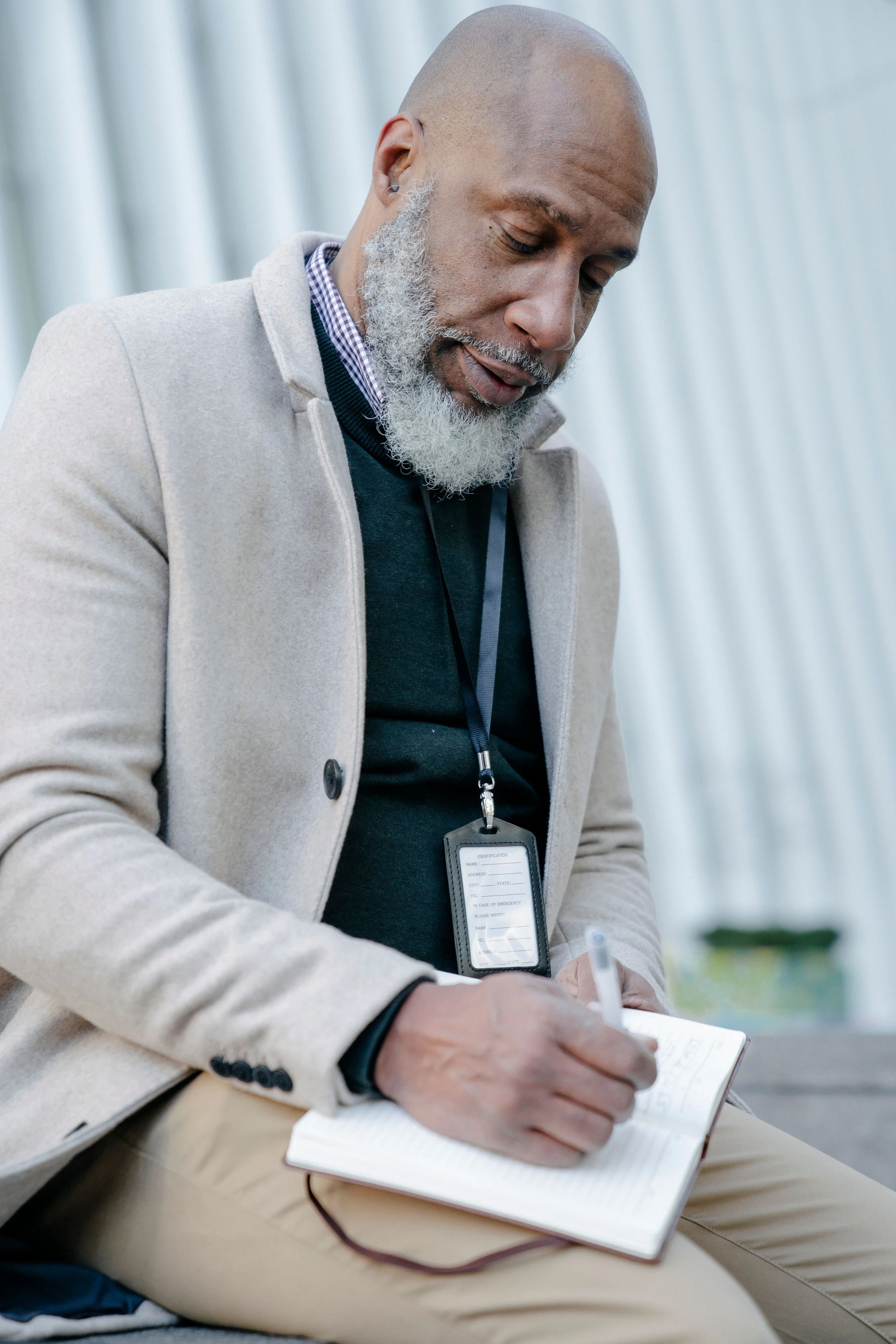 An older man sitting on a bench outdoors and writing in a notebook.