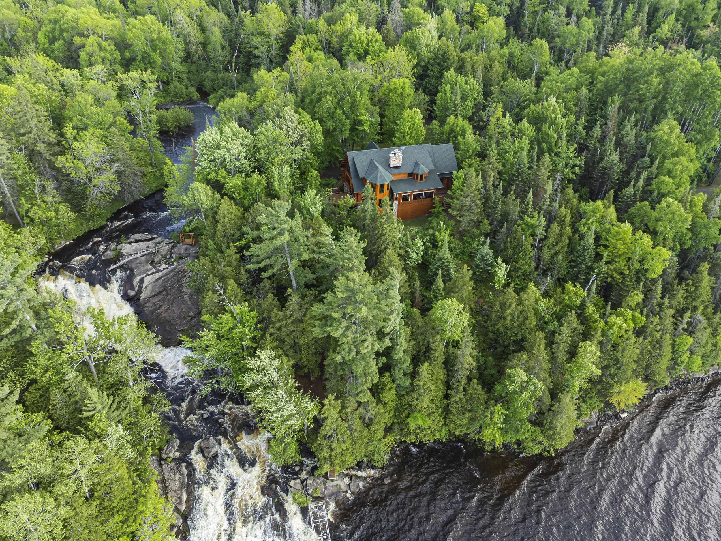 Aerial view of the Gem Falls lodge beside a waterfall and forested shoreline