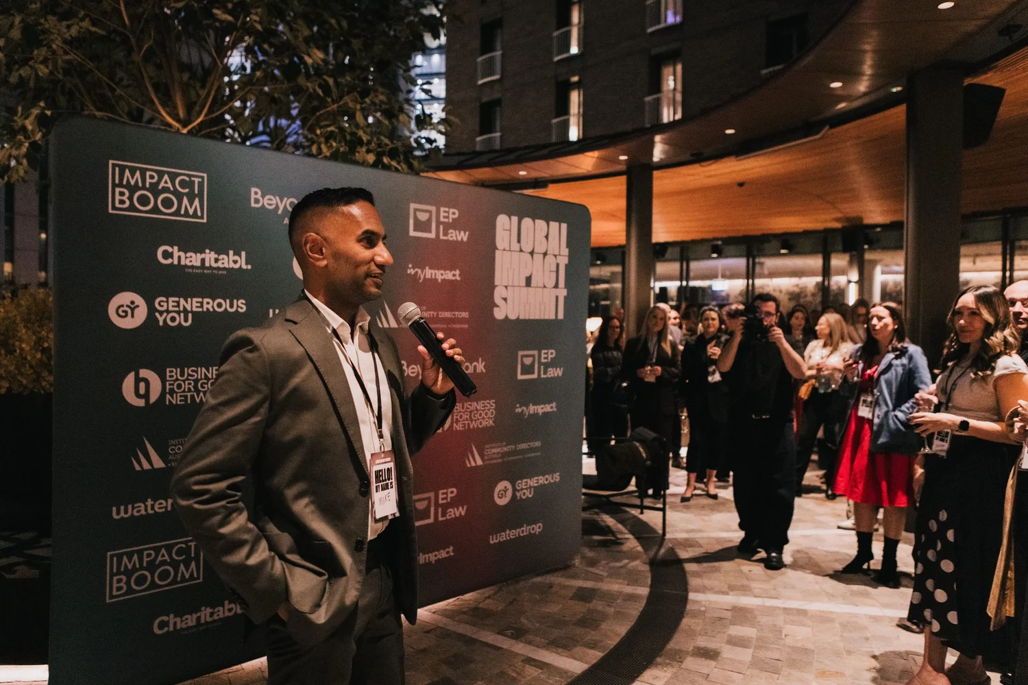 A speaker with a microphone addressing guests at the launch party in front of the Summit backdrop