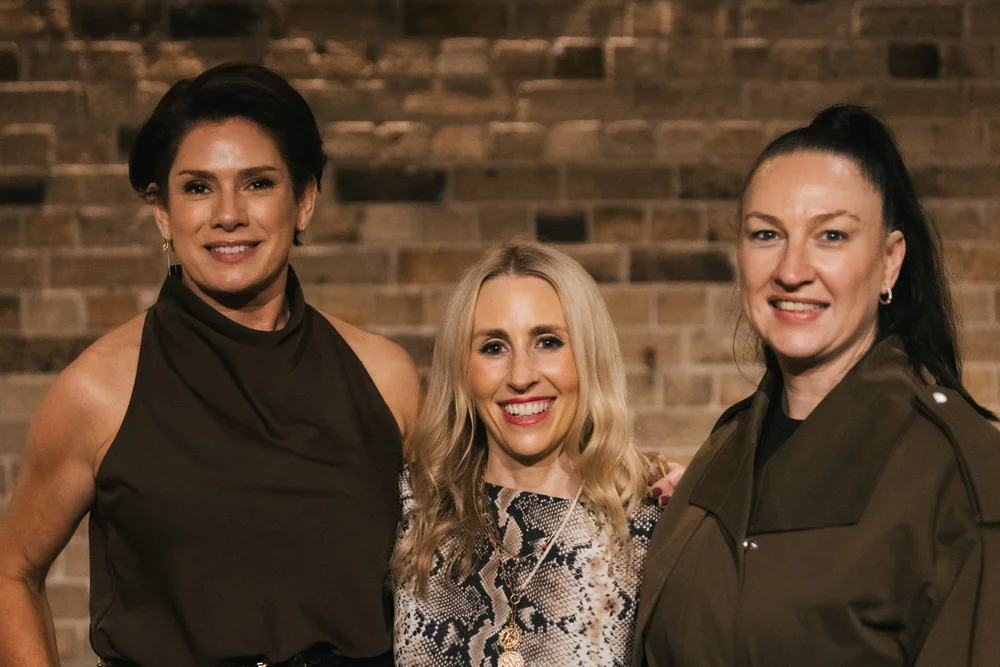 Three guests smiling together against a sandstone wall at the VIP dinner