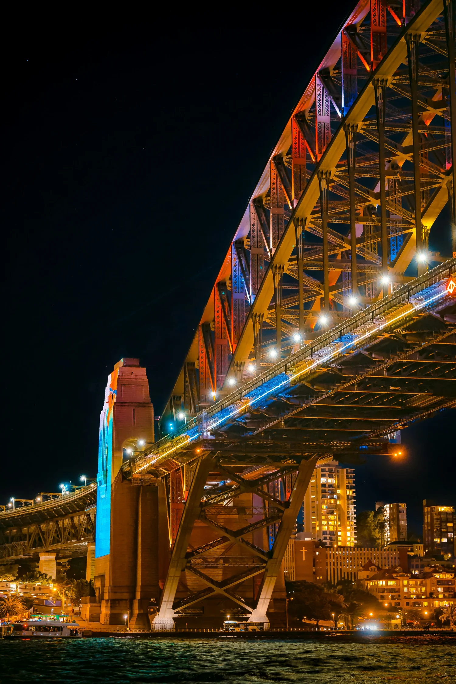 The Sydney Harbour Bridge lit up at night, seen from the water below